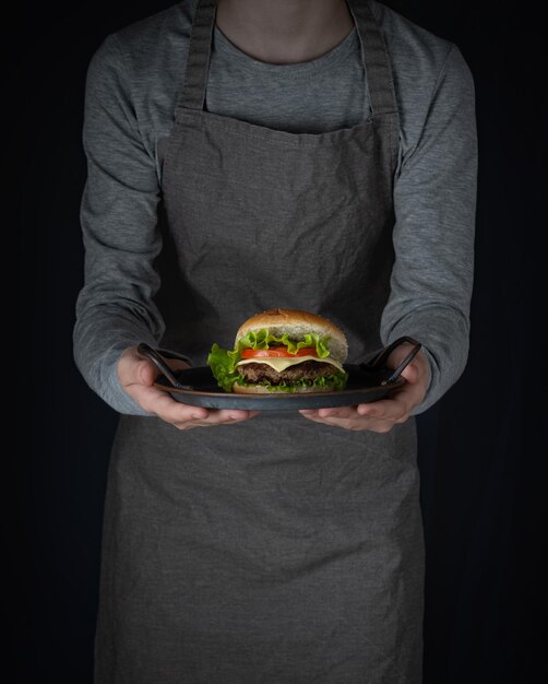 Femme en tablier tenant dans ses mains un plateau avec burger