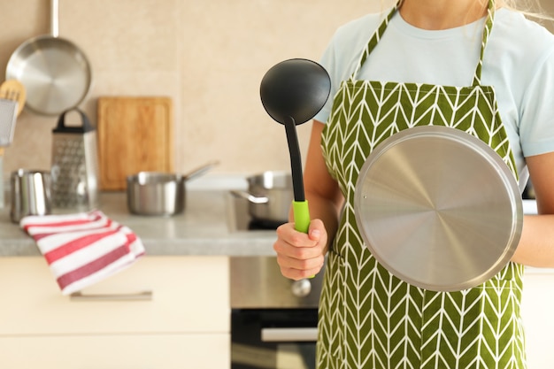 Une femme en tablier tient une louche de cuisine et un capuchon de casserole.