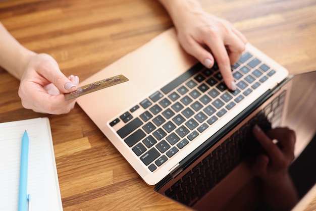 Femme tapant sur un clavier d'ordinateur portable et tenant une carte de crédit bancaire en gros plan