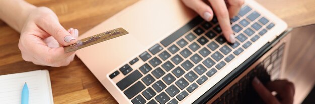 Femme tapant sur un clavier d'ordinateur portable et tenant une carte de crédit bancaire en gros plan