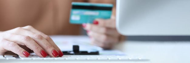 Photo femme tapant sur le clavier de l'ordinateur et tenant une carte bancaire dans ses mains en gros plan