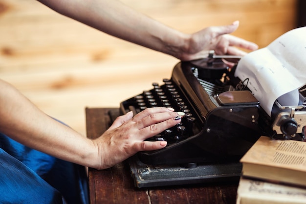 Femme tapant sur la machine à écrire vintage avec du papier vierge sur un bureau en bois