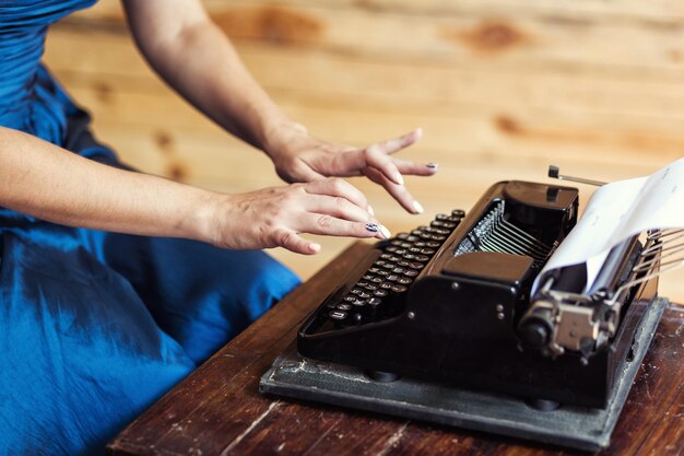 Femme tapant sur la machine à écrire vintage avec du papier vierge sur un bureau en bois