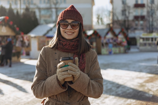 femme avec une tasse de boisson chaude à emporter debout sur la place à la Foire de Noël