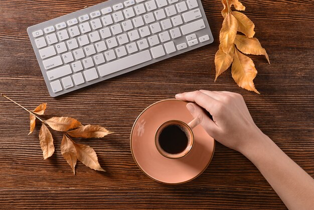 Femme avec une tasse de café aromatique et un clavier d'ordinateur à table, vue de dessus