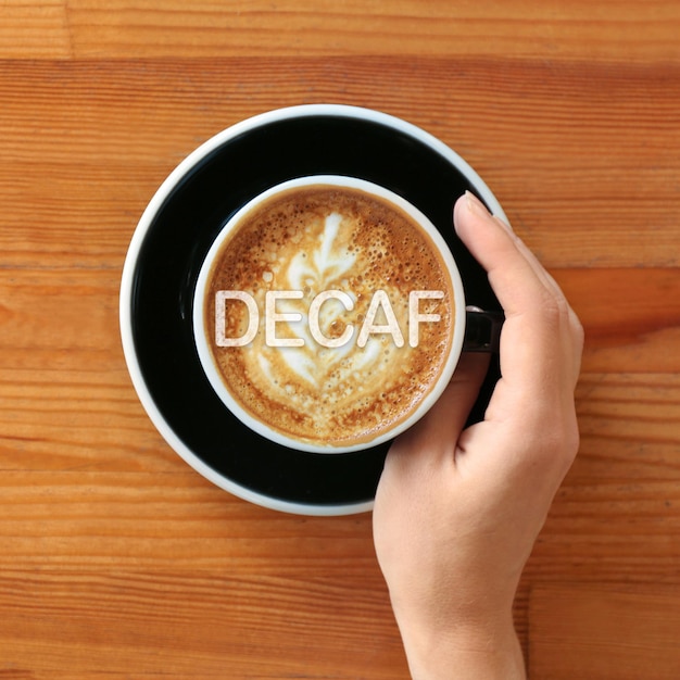 Femme avec une tasse de café décaféiné aromatique à la vue de dessus de table en bois