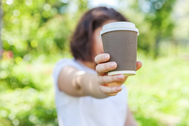 Femme avec une tasse de café à emporter reposant sur un parc ou un fond vert de jardin.