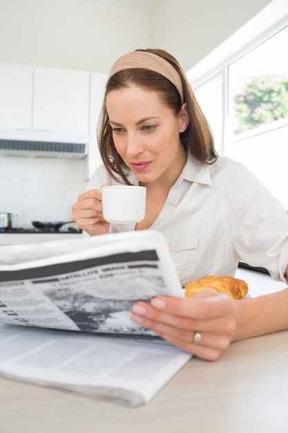 Femme avec une tasse de café en lisant le journal dans la cuisine