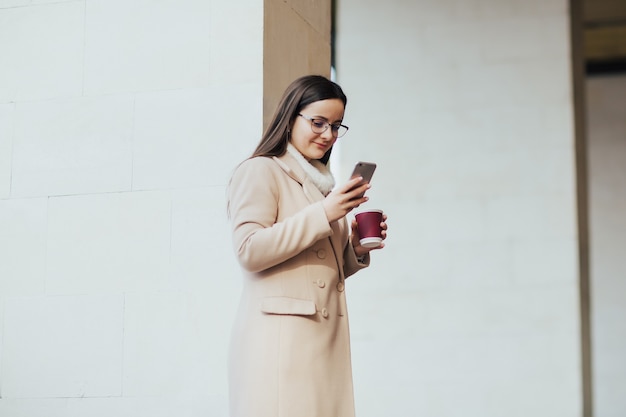 femme, à, tasse café, et, smartphone, debout, près, bâtiment