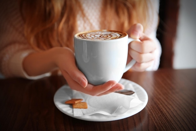Femme avec une tasse de cappuccino sur table au café