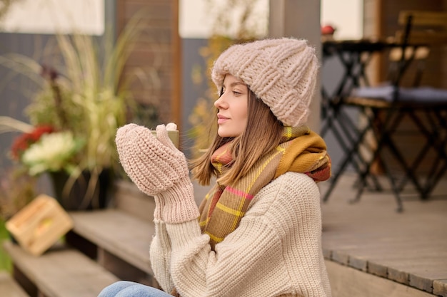 Femme avec une tasse sur le côté de l'appareil photo assis sur la véranda