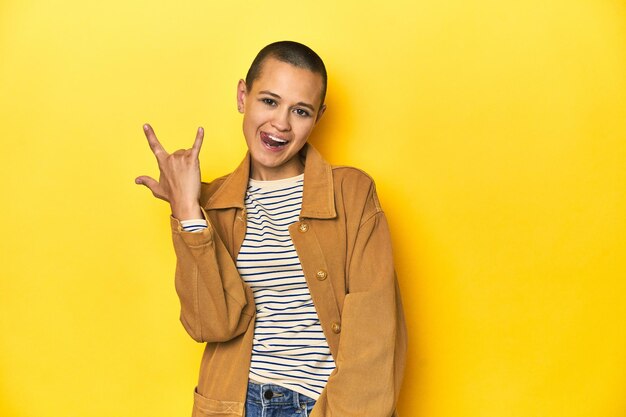 Femme en tee rayé et chemise denim à fond jaune montrant un geste de cornes comme un concept de révolution