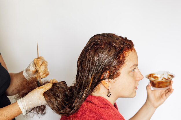 Femme teignant les cheveux de femme en rouge ayant une brosse dans les mains avec des gants en latex blanc sur fond blanc Coloration des cheveux à la maison Se débarrasser des cheveux gris Antiage