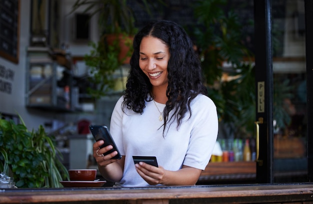 Femme téléphone et carte de crédit avec sourire pour les achats en ligne de commerce électronique ou l'achat au café Bonne cliente sur smartphone pour l'application bancaire sur Internet ou la transaction sans fil au café intérieur