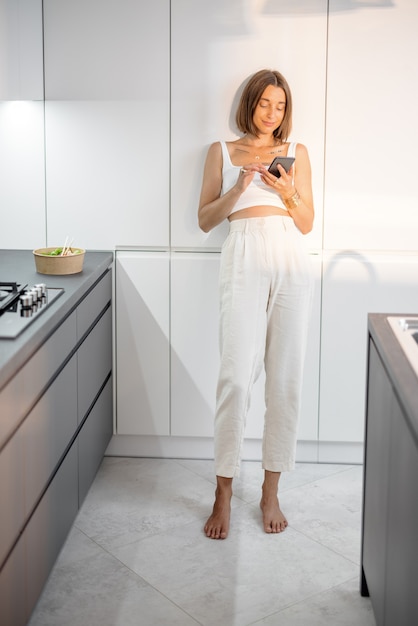 Femme avec téléphone sur la cuisine moderne à la maison