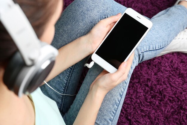 Femme avec un téléphone moderne assis sur le sol Concept de livre audio