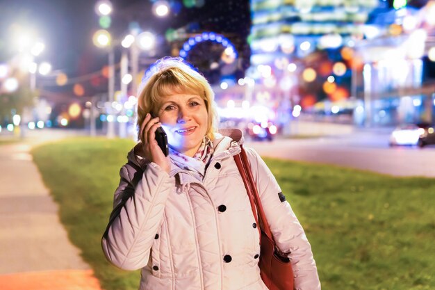 Une femme avec un téléphone portable à la main se promène dans la ville nocturne.