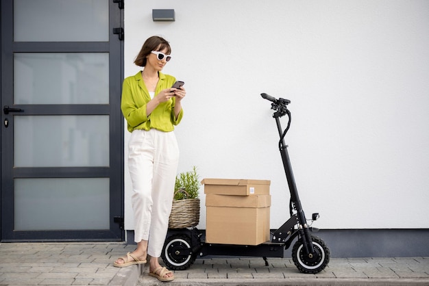 Femme avec téléphone scooter électrique et colis rentrant à la maison