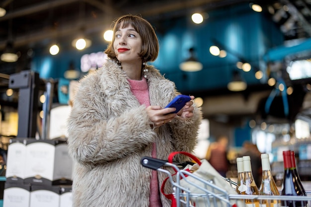 Femme avec téléphone et vin au supermarché