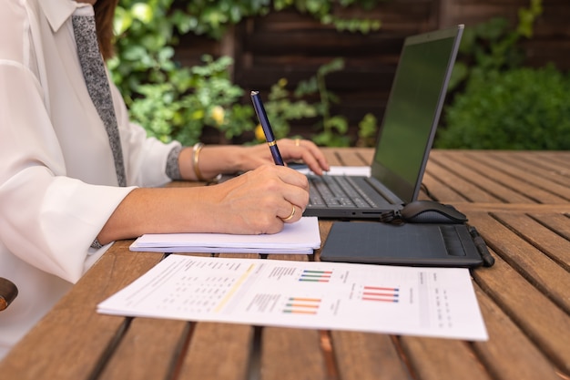 Femme télétravaillant dans le jardin de sa maison et prenant des notes dans un cahier.