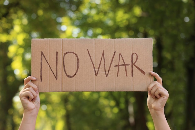 Femme tenant une affiche avec des mots Pas de guerre dans le parc agrandi