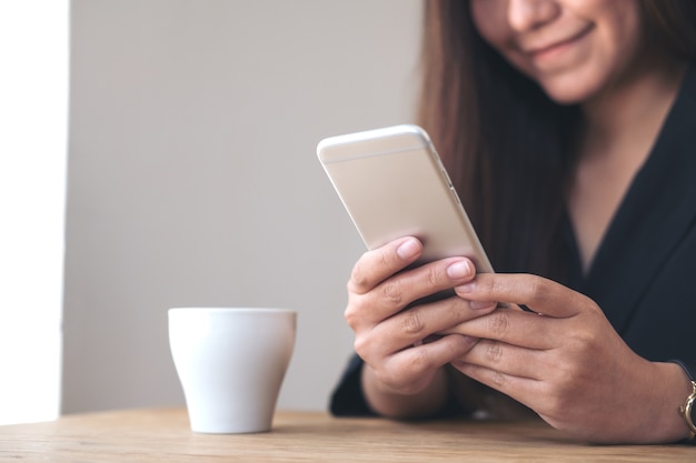 une femme tenant et à l&#39;aide de smartphone avec une tasse de café sur une table en bois dans un café