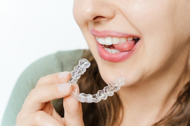 Une femme tenant un aligner dentaire transparent près de la bouche