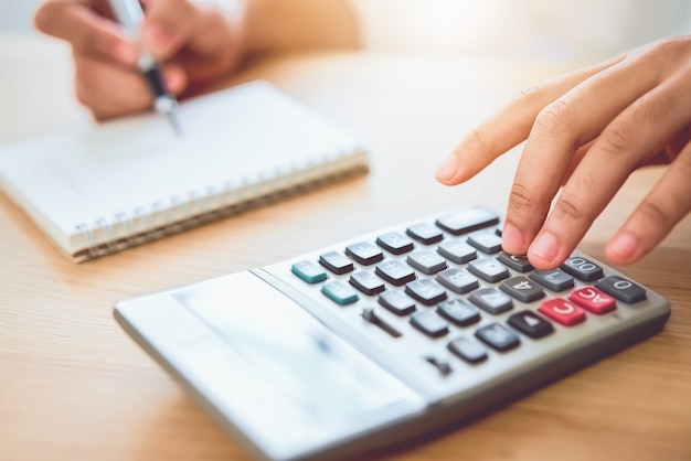 Femme tenant et appuyez sur la calculatrice pour calculer les dépenses de revenu et les plans pour dépenser de l'argent sur le bureau à domicile.