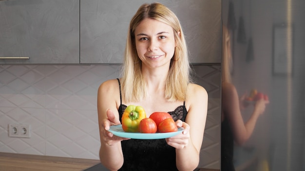 Femme tenant une assiette avec des légumes frais et souriant