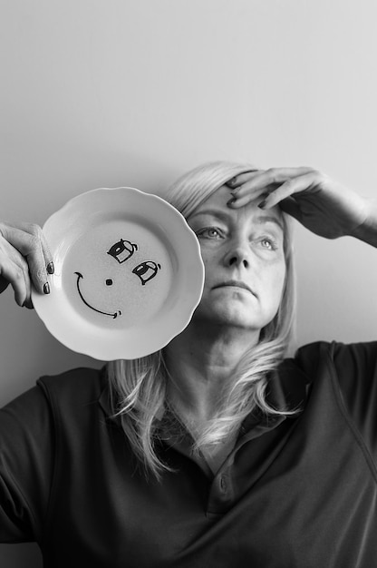 Photo femme tenant une assiette avec un visage souriant contre le mur à la maison