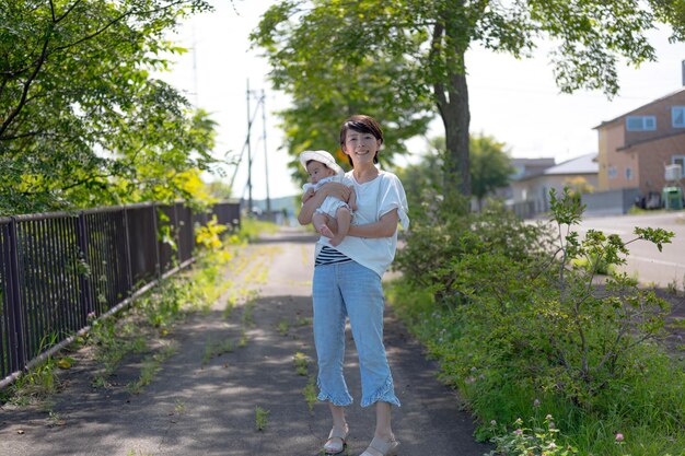 Une femme tenant un bébé se tient sur une route avec des arbres en arrière-plan.