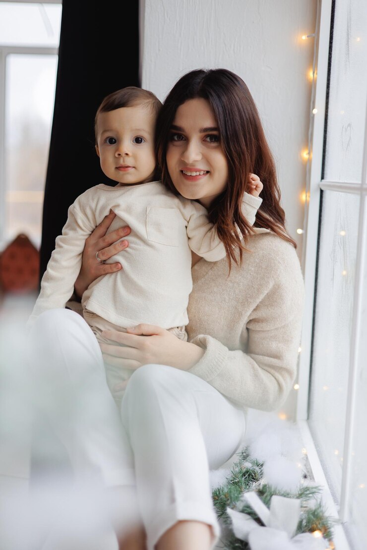 Photo une femme tenant un bébé et souriant devant une fenêtre