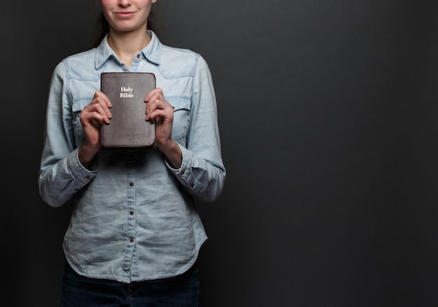 Femme tenant une Bible dans les mains portant des vêtements décontractés sur fond gris