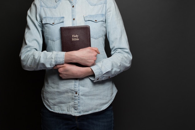 Femme tenant une Bible dans les mains portant des vêtements décontractés sur fond gris