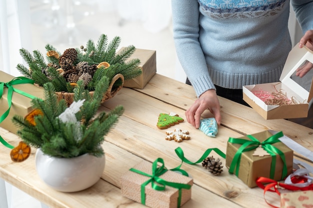 Femme tenant un biscuit de pain d'épice sur une table en bois avec des cadeaux