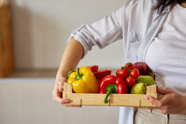 Femme tenant une boîte en bois avec des fruits et légumes frais naturels