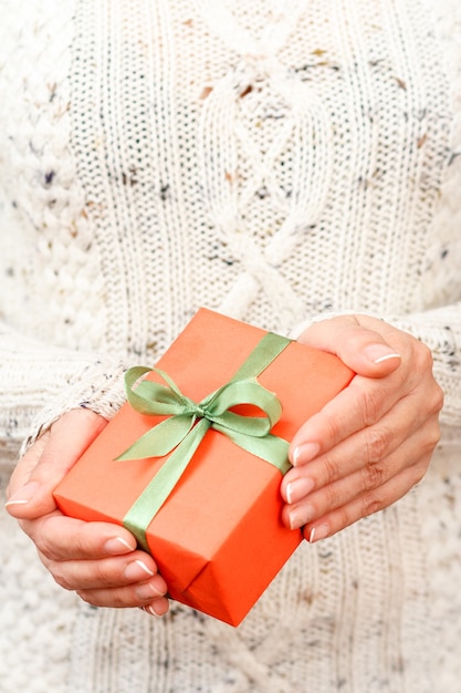 Femme tenant une boîte-cadeau attachée avec un ruban vert dans ses mains. faible profondeur de champ, mise au point sélective sur la boîte. Concept de donner un cadeau en vacances ou anniversaire.