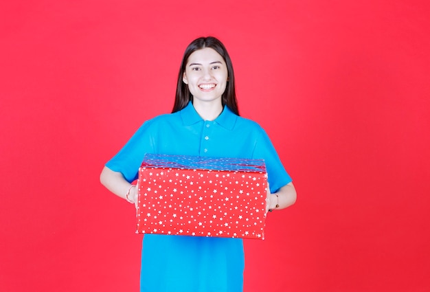 femme tenant une boîte-cadeau rouge avec des points blancs dessus.