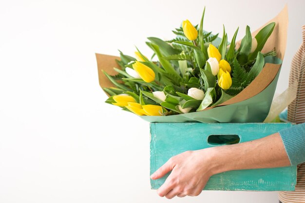 Femme tenant une boîte turquoise rustique avec un bouquet de tulipes jaunes et blanches