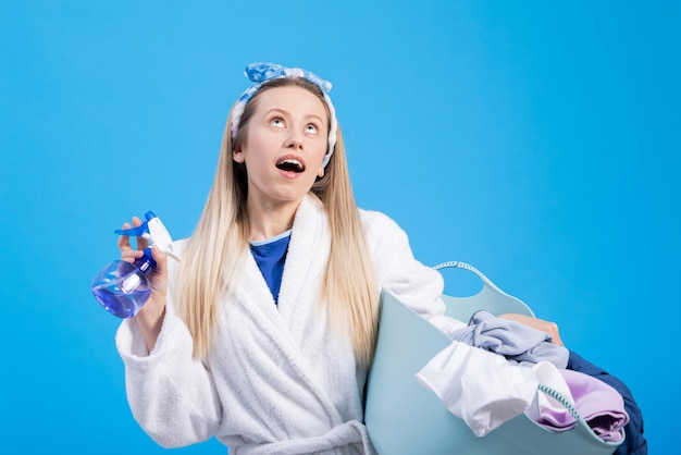 Une femme tenant un bol de linge lève les yeux vers un espace publicitaire vide Portrait de jeune fille sur fond bleu avec des vêtements pour machine à laver