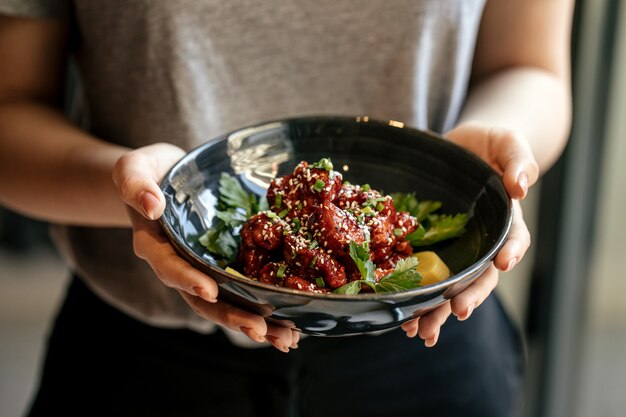 Femme tenant un bol de poulet mariné en sauce épicée avec daikon