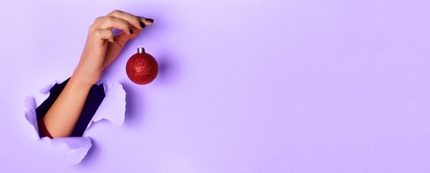 Femme tenant une boule de Noël scintillante rouge à la main sur fond violet