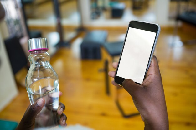 Femme Tenant Une Bouteille D'eau Et à L'aide De Téléphone Portable