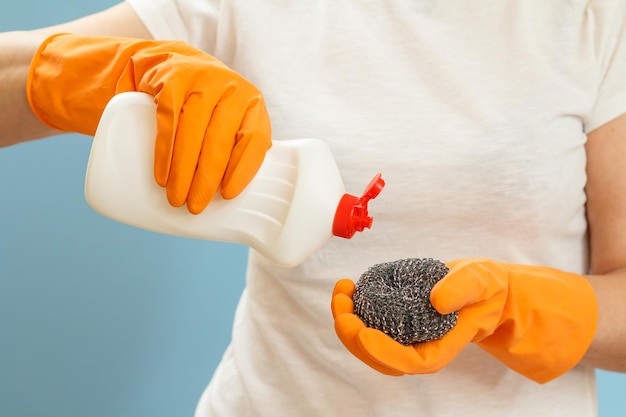 Femme tenant une bouteille de liquide vaisselle et une éponge sur fond bleu