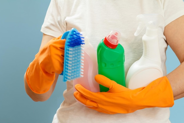 Femme tenant des bouteilles de liquide de lavage et une brosse sur fond bleu