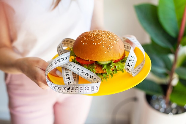 Femme tenant un burger malsain et un ruban à mesurer le concept de perte de poids