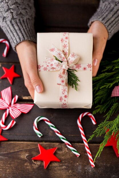 Femme tenant des cadeaux de Noël posés sur un fond de table en bois.