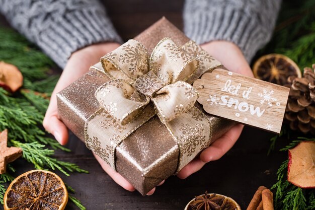 Femme tenant des cadeaux de Noël posés sur un fond de table en bois.