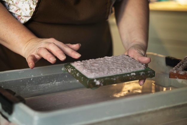 Une femme tenant un cadre pour fabriquer des feuilles de papier à partir de papier recyclé. Mise au point sélective. Passe-temps ménager, recyclage du papier. Le concept de zéro déchet, de recyclage, d'écologie.