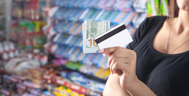 Femme tenant une carte de crédit et de l'argent au supermarché.